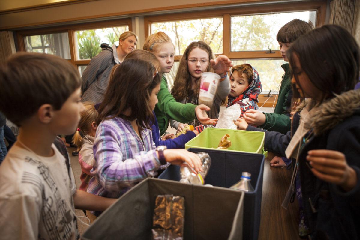 A large group of students is gathered around three waste sorting bins.
